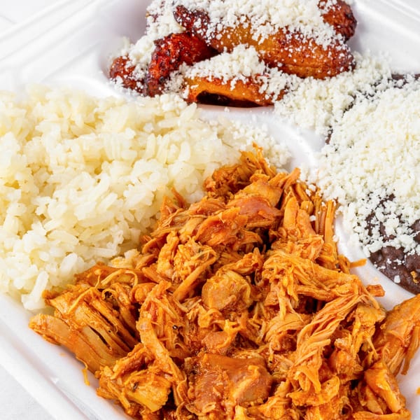 Venezuelan dish with shredded chicken, rice, black beans, fried plantains, and crumbled white cheese.