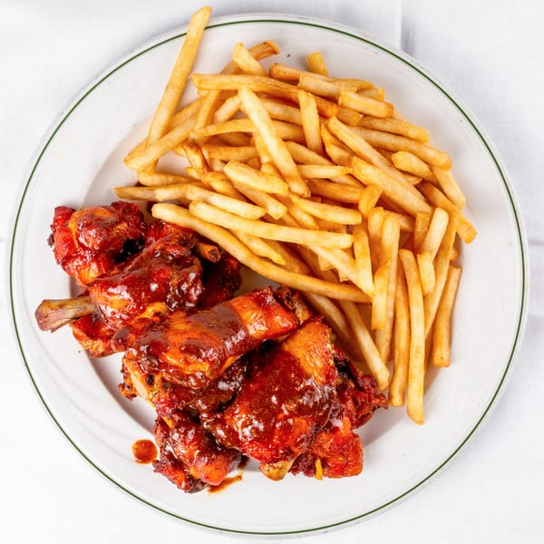 Viva Las Arepas' Venezuelan chicken wings in red sauce with a side of golden french fries.