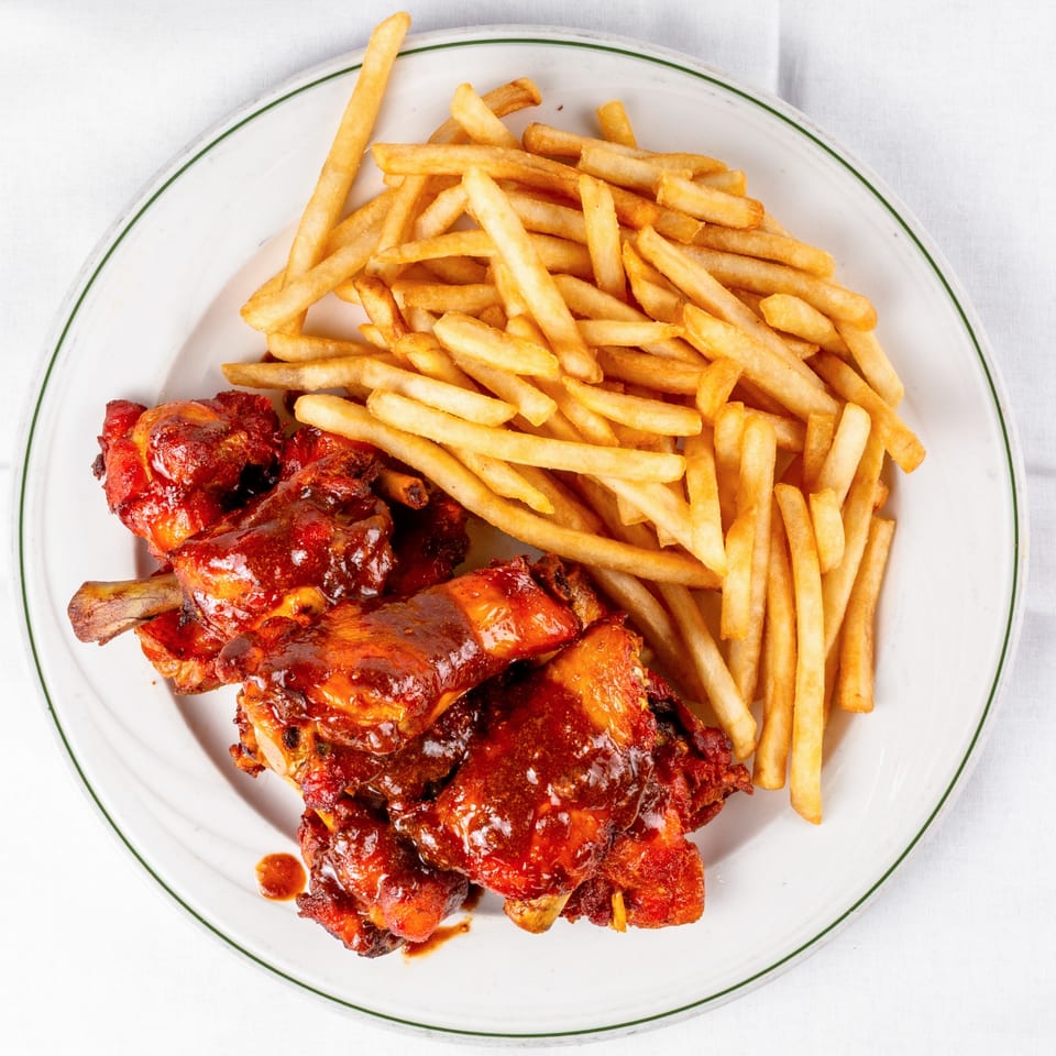 Viva Las Arepas' Venezuelan chicken wings in red sauce with a side of golden french fries.