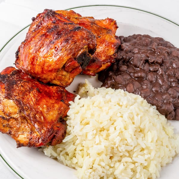 Venezuelan grilled chicken with black beans and white rice on a white plate.