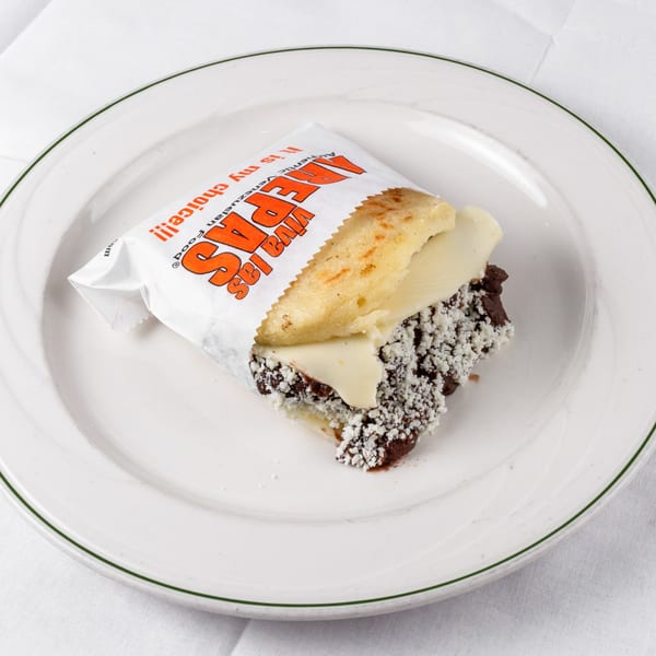 A Viva Las Arepas cachapa with cheese and a dark filling, sprinkled with white cheese, on a white plate.