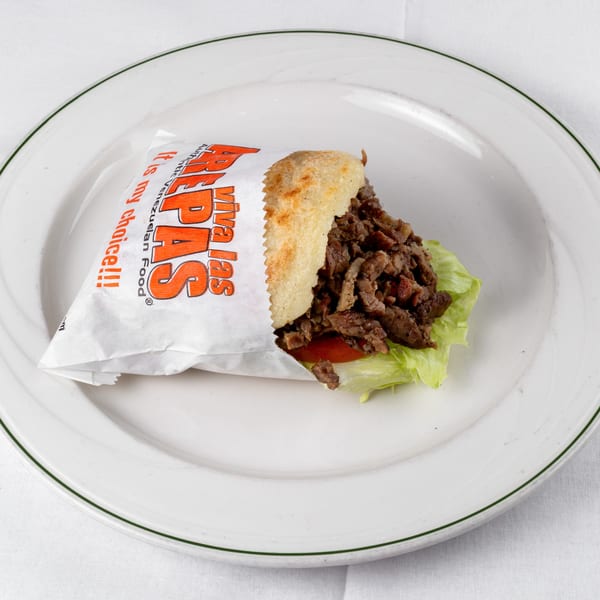 Viva Las Arepas Venezuelan shredded beef and vegetable arepa, partially unwrapped, on a white plate.