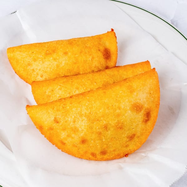 Three golden-fried Venezuelan empanadas, crescent-shaped and crispy, resting on white parchment paper.