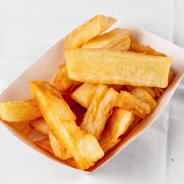 A white paper tray filled with golden-brown, crispy Venezuelan yuca fries on a white tablecloth.