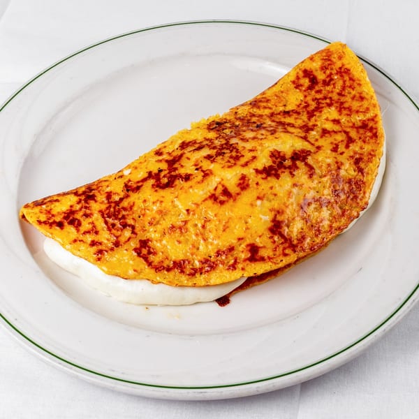 A golden-brown Venezuelan cachapa, folded and filled with white cheese, on a white plate.